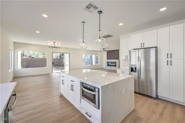 kitchen with visible vents, a glass covered fireplace, appliances with stainless steel finishes, a center island, and white cabinetry