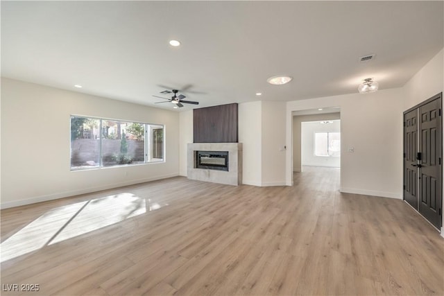 unfurnished living room featuring recessed lighting, visible vents, a glass covered fireplace, light wood-type flooring, and baseboards