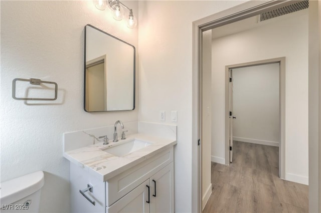 bathroom featuring toilet, wood finished floors, vanity, visible vents, and baseboards