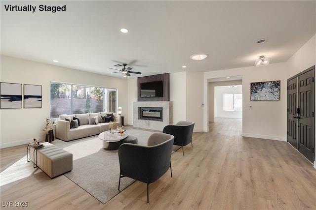 living room with light wood-type flooring, a tile fireplace, visible vents, and baseboards