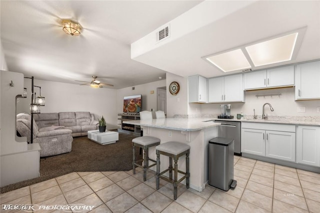 kitchen featuring light tile patterned floors, a breakfast bar, dishwasher, white cabinetry, and kitchen peninsula