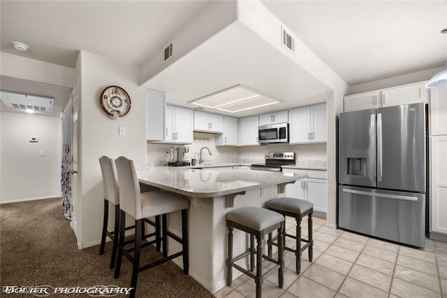 kitchen with white cabinetry, appliances with stainless steel finishes, a kitchen breakfast bar, and kitchen peninsula