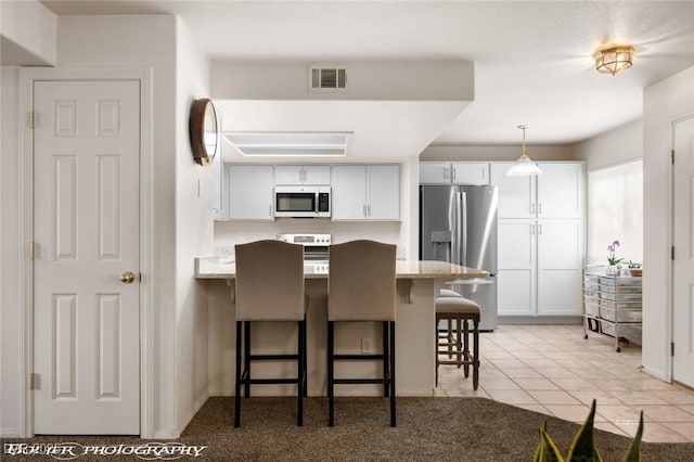 kitchen with a breakfast bar area, appliances with stainless steel finishes, hanging light fixtures, light stone countertops, and white cabinets