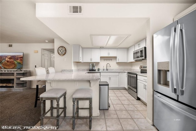 kitchen with a kitchen bar, white cabinetry, light stone counters, kitchen peninsula, and stainless steel appliances