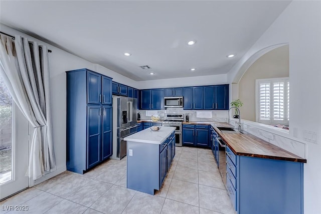 kitchen with a kitchen island, appliances with stainless steel finishes, blue cabinets, sink, and light tile patterned floors