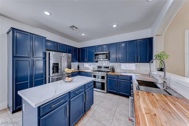 kitchen featuring light tile patterned flooring, blue cabinets, sink, appliances with stainless steel finishes, and light stone countertops