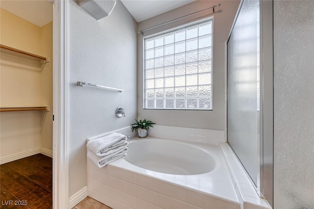 bathroom with a relaxing tiled tub and wood-type flooring