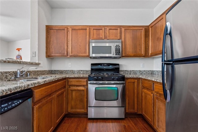 kitchen with appliances with stainless steel finishes, dark hardwood / wood-style floors, light stone countertops, and sink