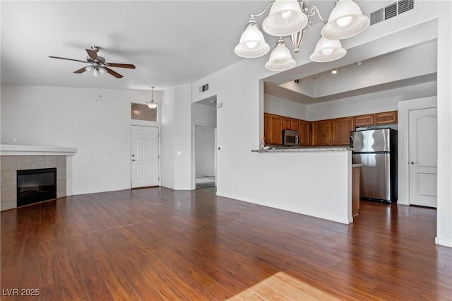 unfurnished living room featuring dark hardwood / wood-style floors, a tiled fireplace, and ceiling fan with notable chandelier