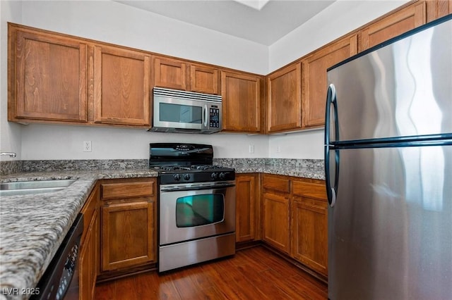 kitchen with sink, dark wood-type flooring, stainless steel appliances, and stone counters