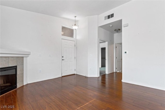 unfurnished living room featuring dark hardwood / wood-style flooring, a tiled fireplace, and a towering ceiling