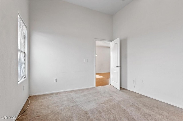 spare room featuring a towering ceiling and light colored carpet