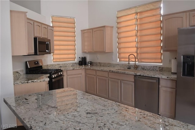 kitchen with a sink, appliances with stainless steel finishes, light brown cabinets, and light stone countertops
