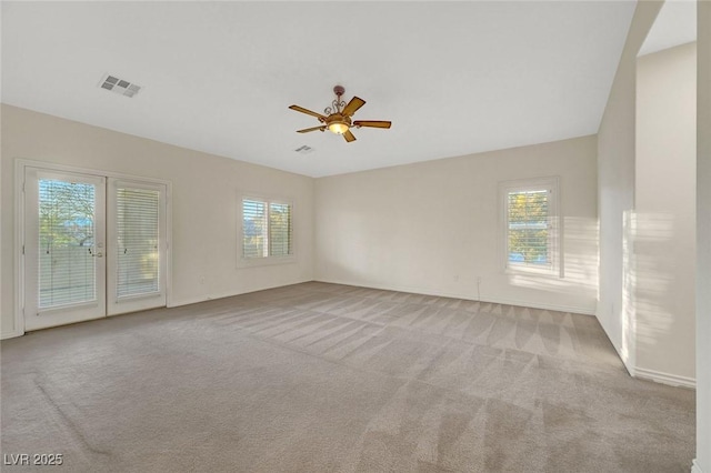 spare room with light colored carpet, visible vents, ceiling fan, and baseboards