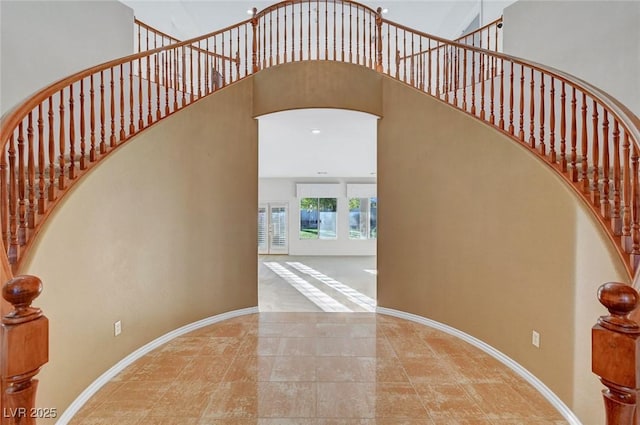 stairs featuring arched walkways, a towering ceiling, and baseboards