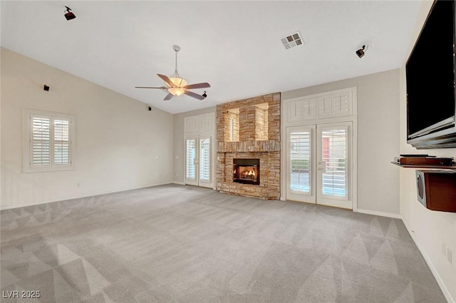 unfurnished living room with light colored carpet, a wealth of natural light, visible vents, and a stone fireplace