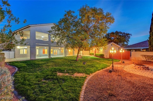 rear view of property with a patio, an outdoor fire pit, fence, a yard, and stucco siding