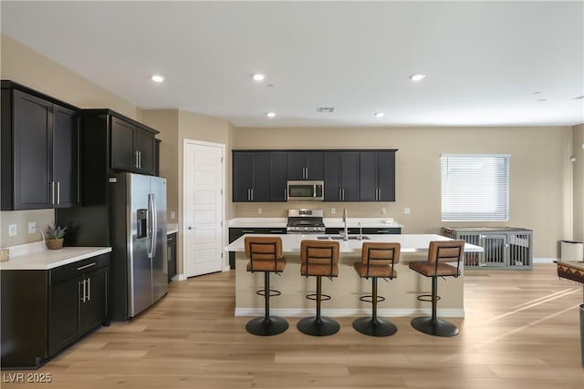 kitchen featuring a breakfast bar, sink, a center island with sink, appliances with stainless steel finishes, and light hardwood / wood-style floors