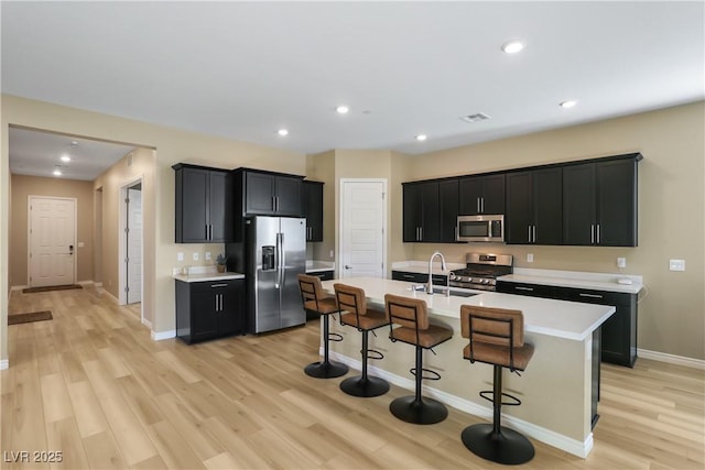 kitchen with sink, a breakfast bar area, stainless steel appliances, an island with sink, and light wood-type flooring