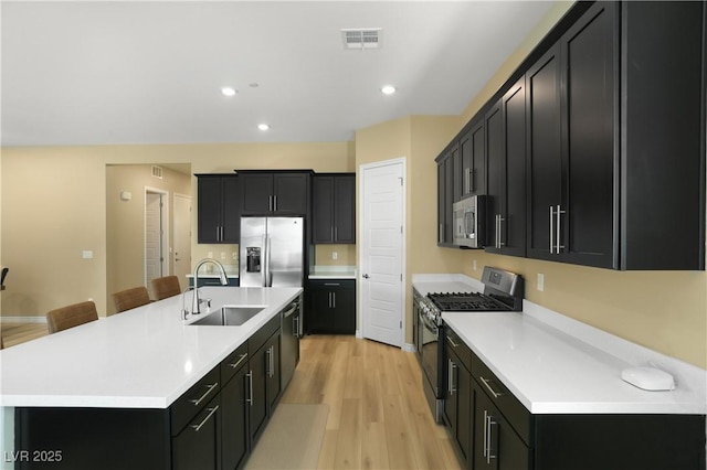 kitchen featuring sink, a breakfast bar area, appliances with stainless steel finishes, light hardwood / wood-style floors, and an island with sink