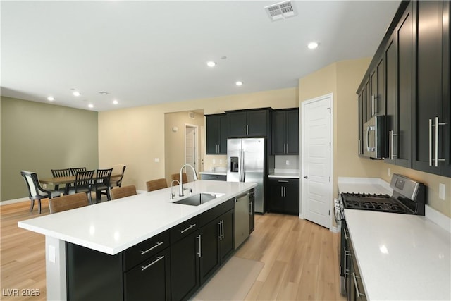 kitchen featuring a breakfast bar, sink, a center island with sink, light wood-type flooring, and stainless steel appliances