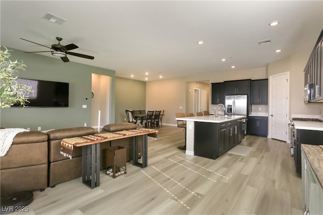 kitchen with sink, a breakfast bar area, light wood-type flooring, appliances with stainless steel finishes, and a kitchen island with sink