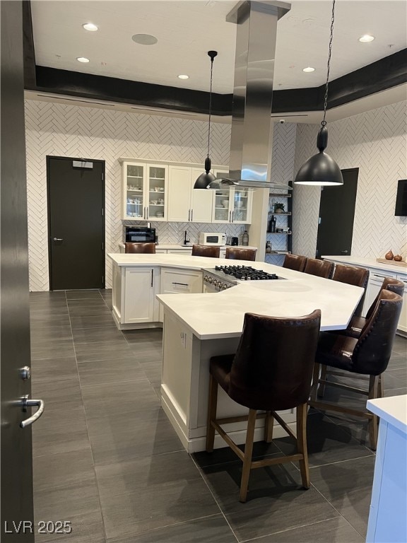 kitchen featuring a breakfast bar, a kitchen island, white cabinets, island exhaust hood, and decorative light fixtures