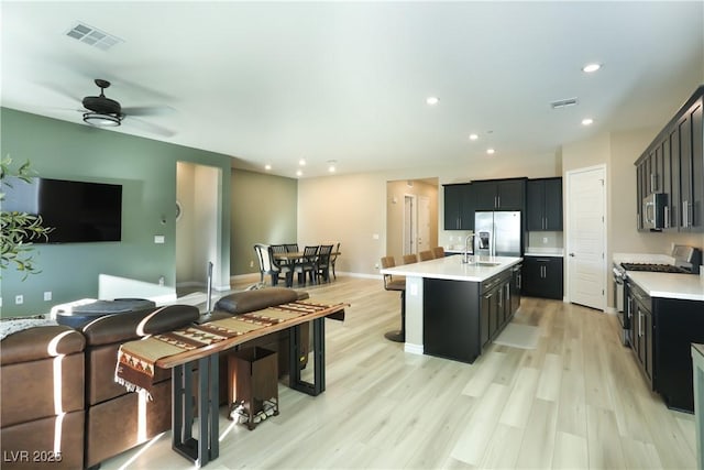 kitchen with light hardwood / wood-style flooring, ceiling fan, appliances with stainless steel finishes, a kitchen island with sink, and a kitchen bar