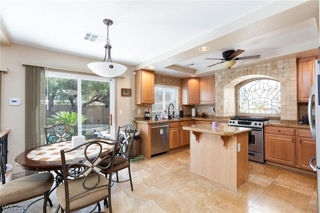 kitchen featuring appliances with stainless steel finishes, hanging light fixtures, a tray ceiling, a kitchen island, and decorative backsplash