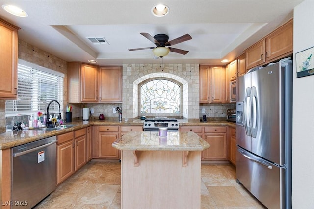 kitchen with sink, a breakfast bar, stainless steel appliances, a tray ceiling, and a kitchen island