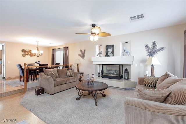 living room with a tiled fireplace and ceiling fan with notable chandelier