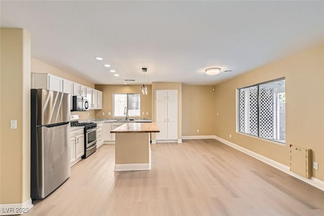 kitchen featuring decorative light fixtures, white cabinetry, a center island, light hardwood / wood-style floors, and stainless steel appliances