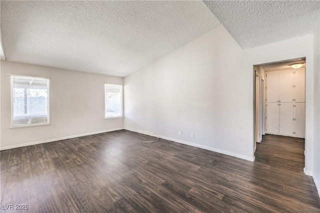 empty room with dark wood finished floors, plenty of natural light, a textured ceiling, and baseboards