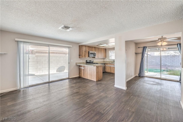 kitchen with visible vents, brown cabinets, appliances with stainless steel finishes, a peninsula, and dark wood-style flooring