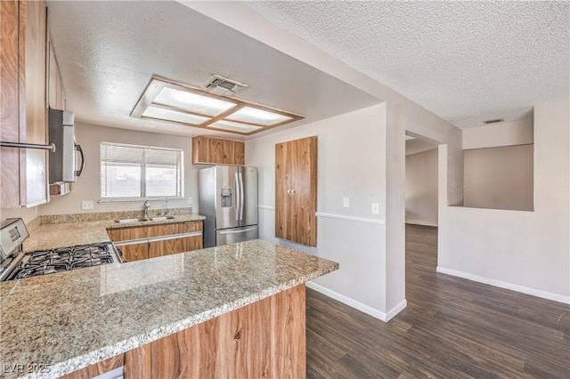 kitchen with visible vents, brown cabinets, a sink, stainless steel appliances, and light stone countertops