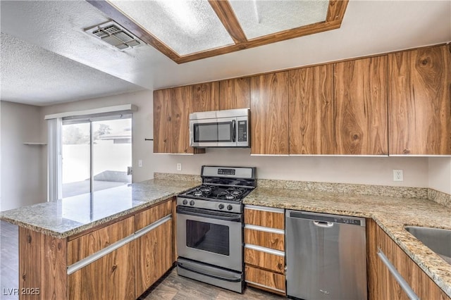 kitchen featuring a peninsula, brown cabinets, visible vents, and stainless steel appliances