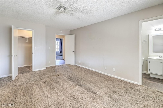 unfurnished bedroom featuring visible vents, carpet floors, ensuite bath, a spacious closet, and a textured ceiling