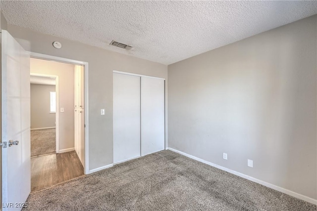 unfurnished bedroom featuring visible vents, baseboards, carpet flooring, a closet, and a textured ceiling