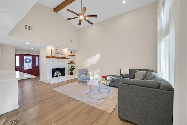 living room featuring high vaulted ceiling, a fireplace, beamed ceiling, hardwood / wood-style flooring, and ceiling fan