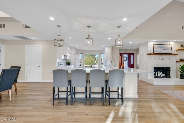 kitchen featuring light hardwood / wood-style flooring, white cabinetry, hanging light fixtures, a fireplace, and a kitchen bar