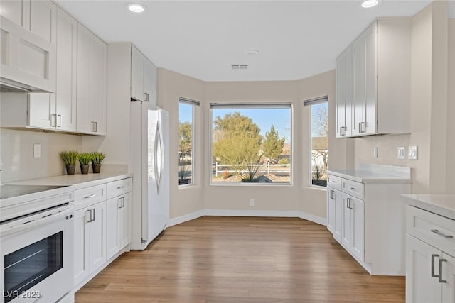 kitchen with white cabinets, white appliances, and light hardwood / wood-style flooring