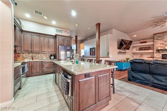 kitchen with appliances with stainless steel finishes, an island with sink, sink, backsplash, and a kitchen bar