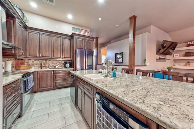 kitchen featuring sink, wall chimney range hood, stainless steel appliances, light stone counters, and decorative backsplash