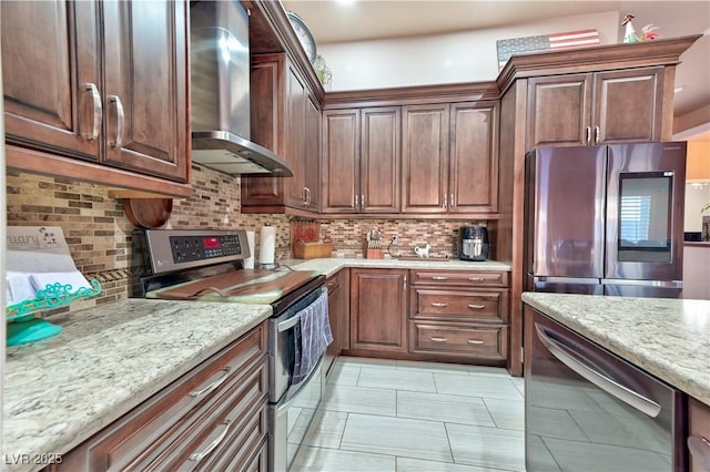 kitchen featuring tasteful backsplash, appliances with stainless steel finishes, light stone counters, and wall chimney range hood