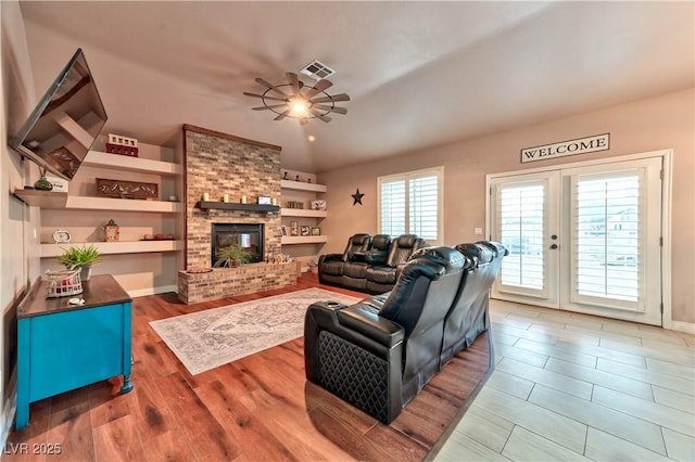 living room with hardwood / wood-style flooring, ceiling fan, a brick fireplace, built in shelves, and french doors