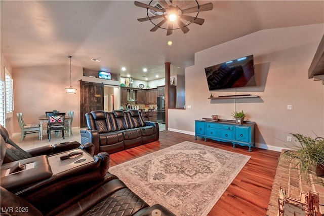 living room with hardwood / wood-style flooring, ceiling fan, a barn door, and vaulted ceiling