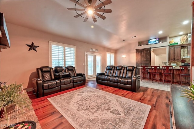 living room featuring vaulted ceiling, a barn door, ceiling fan, and light hardwood / wood-style flooring