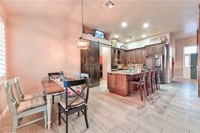 kitchen featuring a kitchen breakfast bar, decorative light fixtures, high end refrigerator, a barn door, and wall chimney exhaust hood