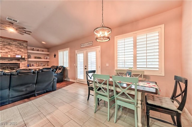 dining area with vaulted ceiling, a brick fireplace, a notable chandelier, and french doors