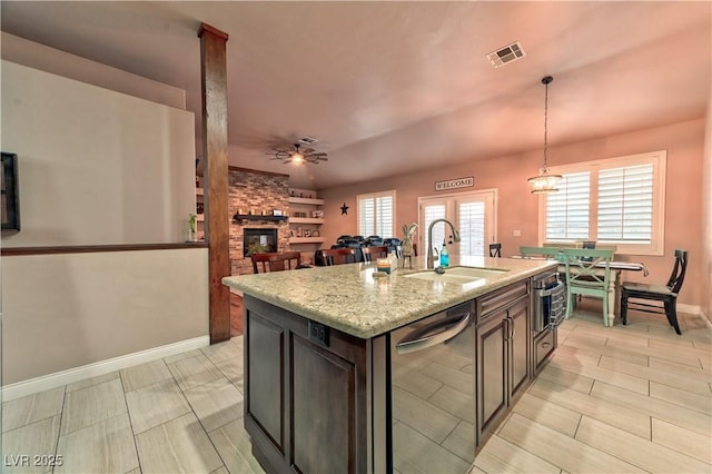 kitchen with sink, a kitchen island with sink, hanging light fixtures, stainless steel appliances, and light stone countertops